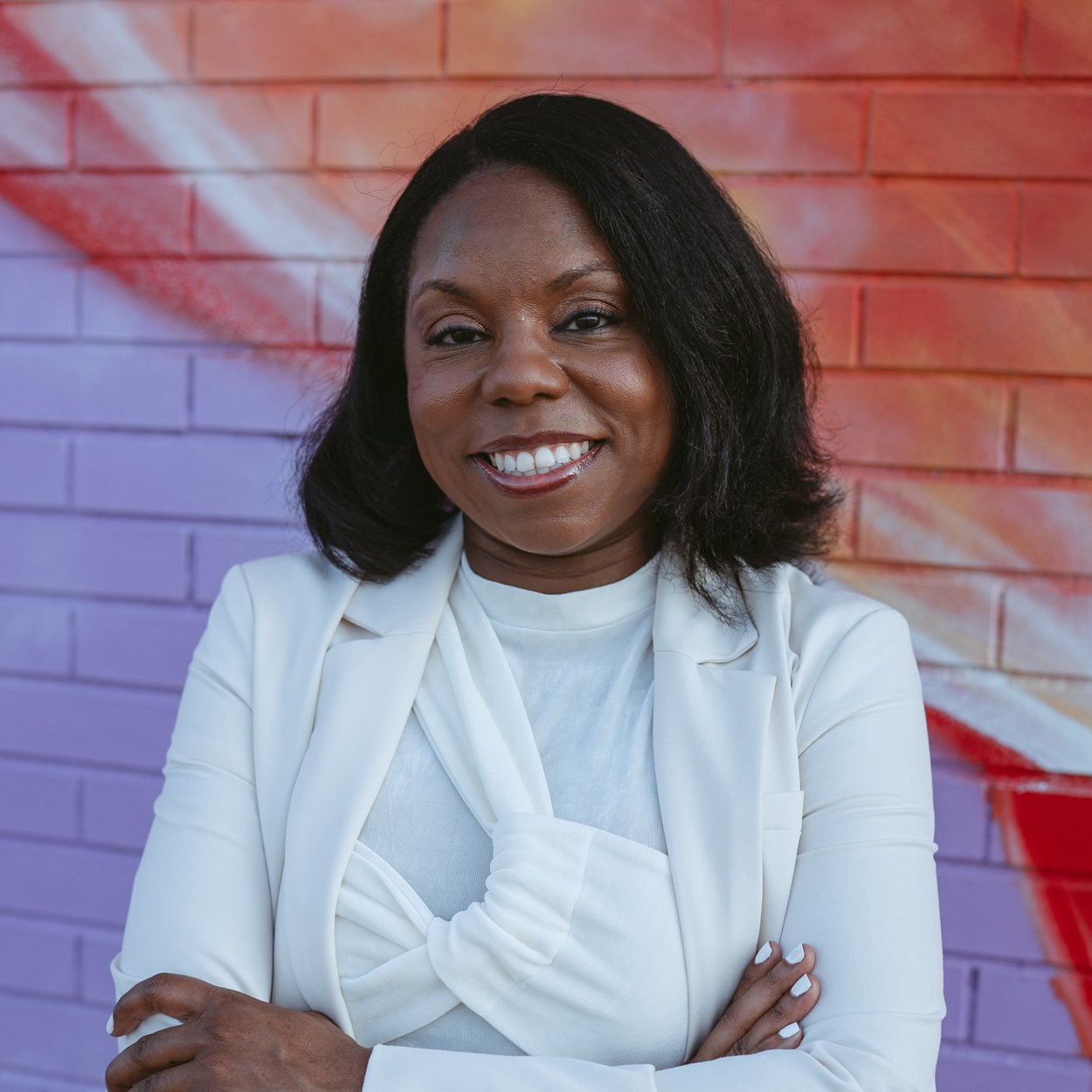 Talisha Searcy wearing white, stands in front of colorful brick wall.